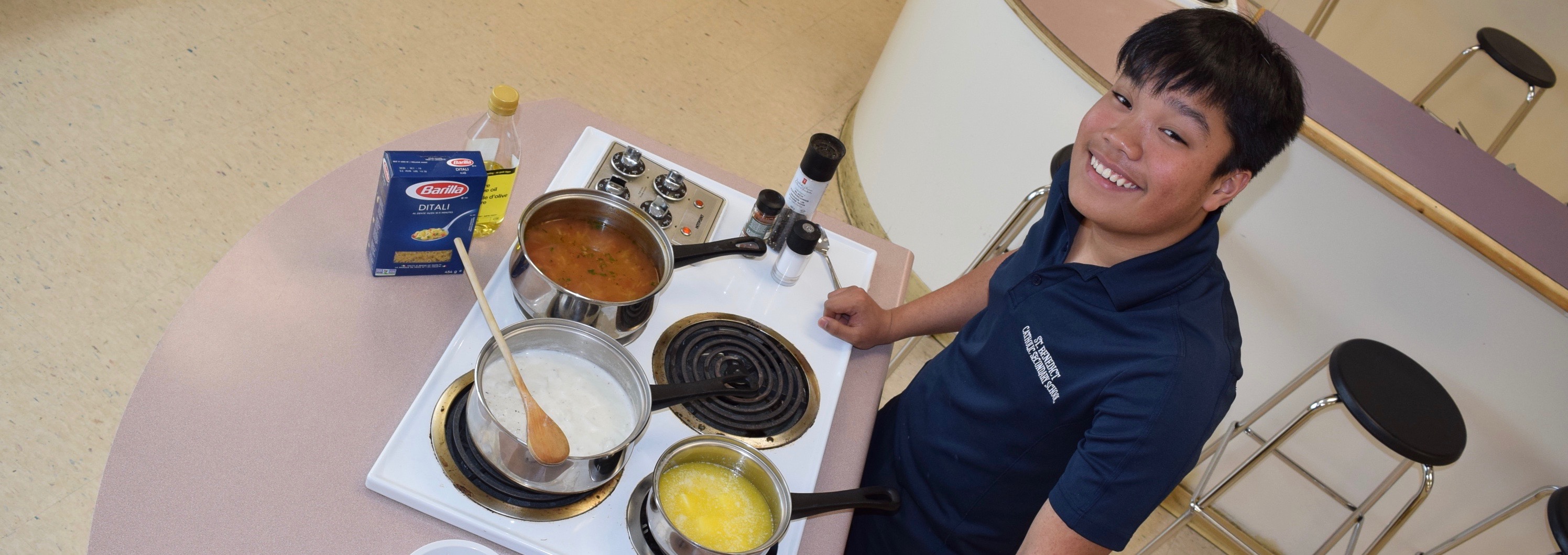 Aivan Apan stands smiling in a kitchen surrounded by cooking utensils and equipment.