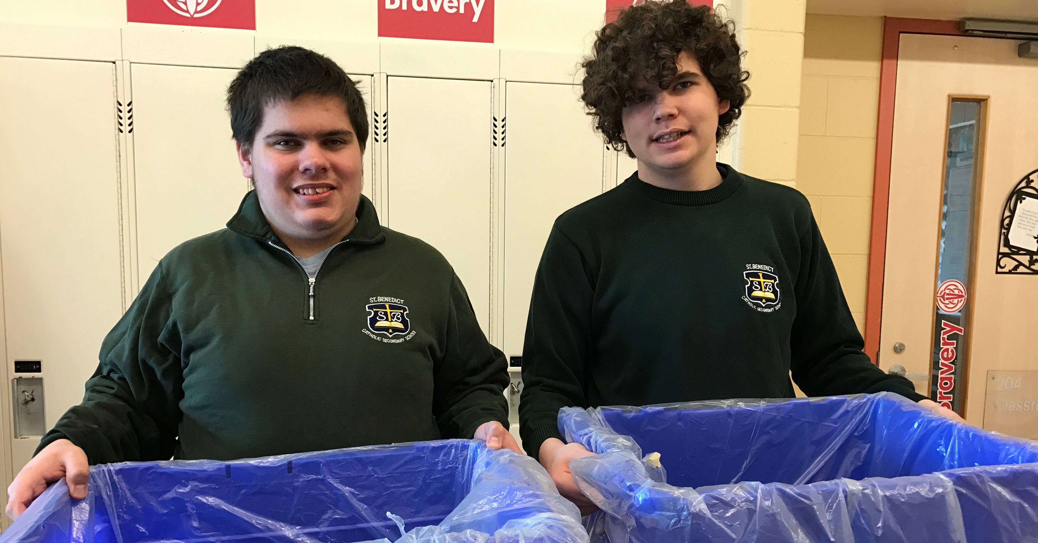 Two lifeskills students at St.Benedict stand smiling while holding two recycling containers.