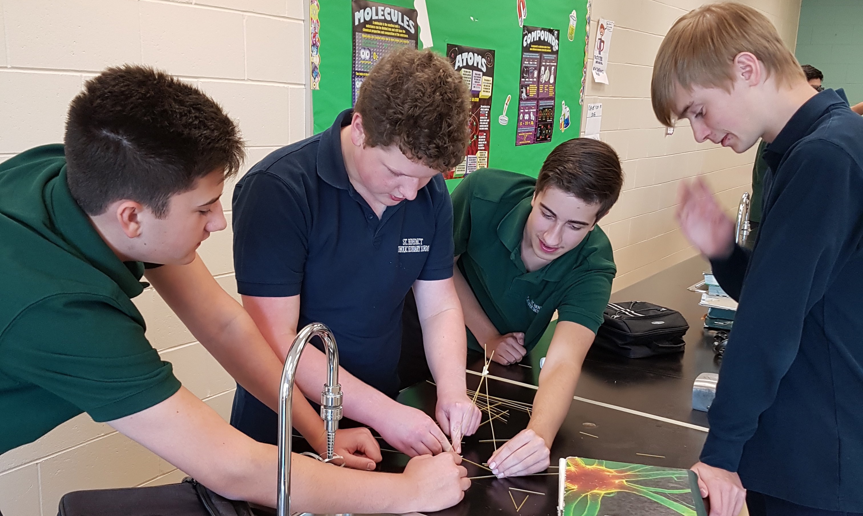 Four boys gather in a science classroom to complete an experiment involving marshmallows and spaghetti.