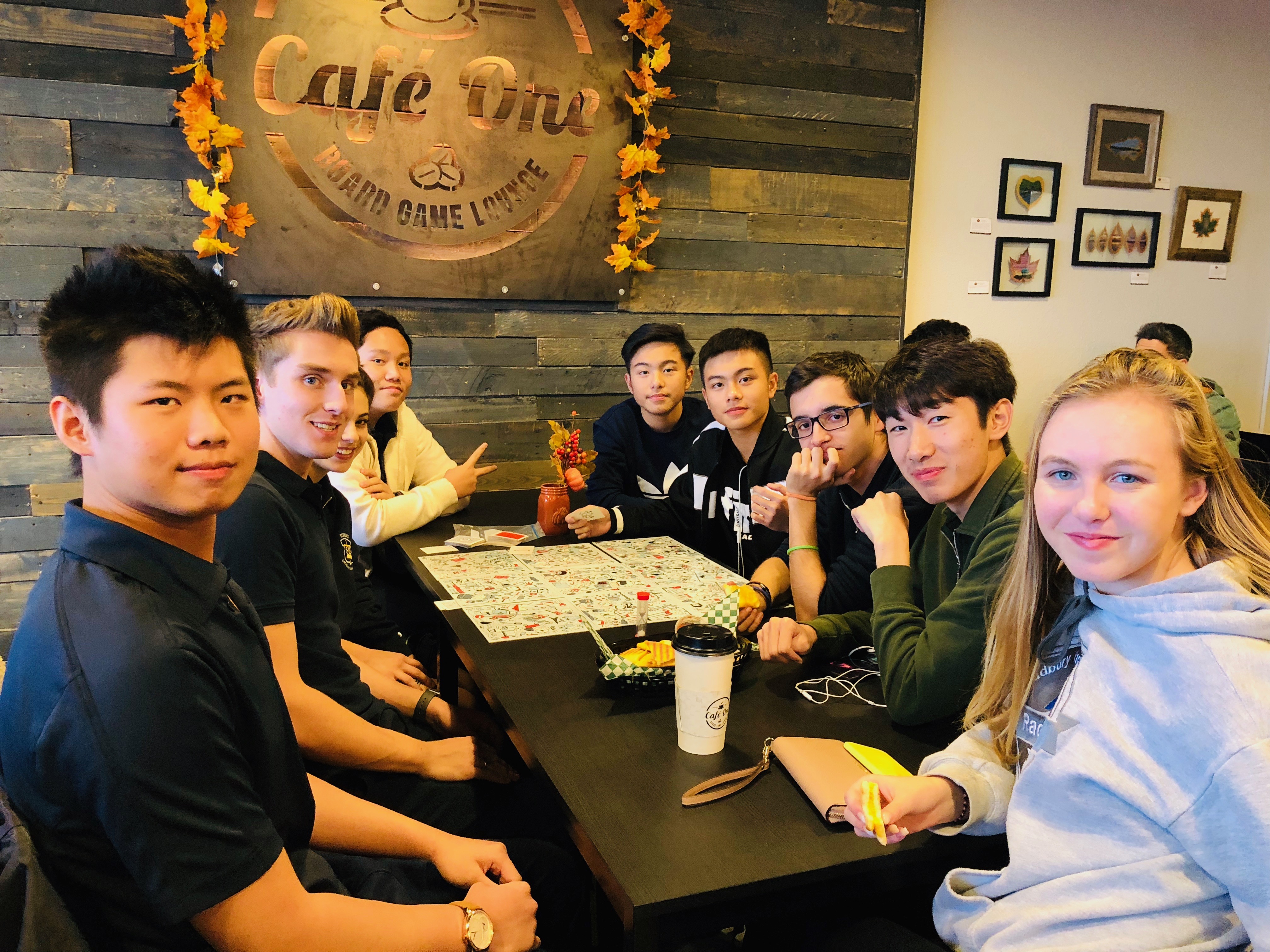 A group of students sit at a table playing a boardgame and laughing.